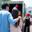 Couple stands by an open moving truck as movers load cardboard boxes inside the trailer.